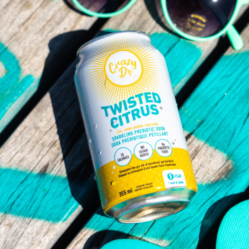 Crazy D's Twisted Citrus sparkling probiotic soda can on a turquoise surface with sunglasses in the background.