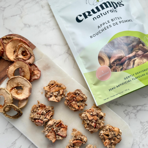 Bag of Crumps Naturals Apple Bites on a marble surface with dried apple slices and treats.