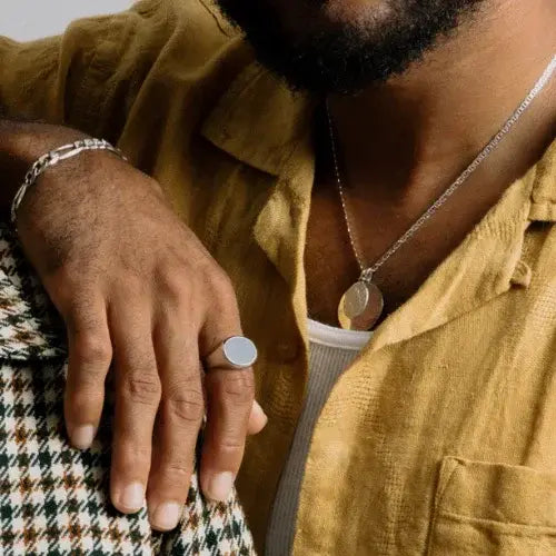 Person wearing a mustard yellow shirt with jewelry including a ring and necklace.