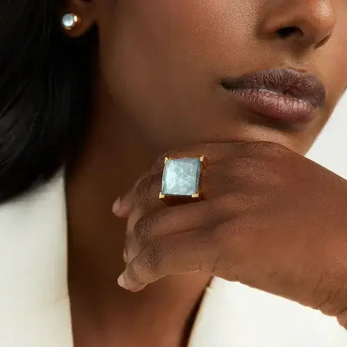 Close-up of a woman wearing a gold ring with a square gemstone on her hand.