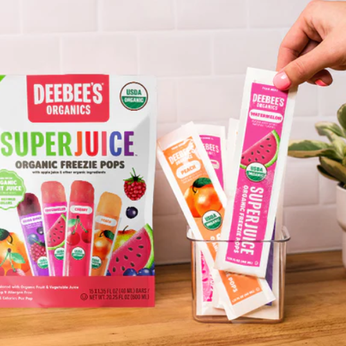 Hand holding a Deebee's Organics Super Juice freezie pop package with popsicles in the background.