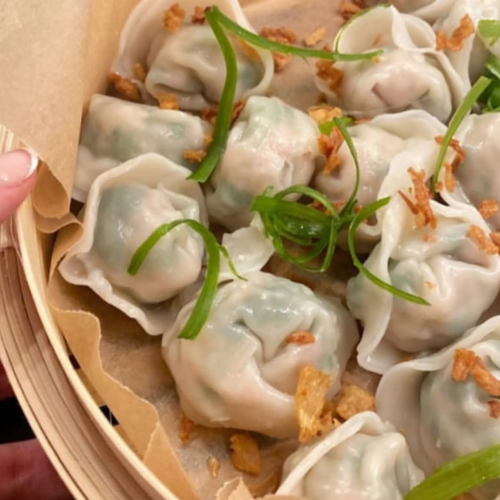 Steamed dumplings with green onions in a bamboo steamer basket