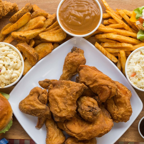 Platter of fried chicken with sides including fries, macaroni and cheese, and coleslaw on a wooden table.