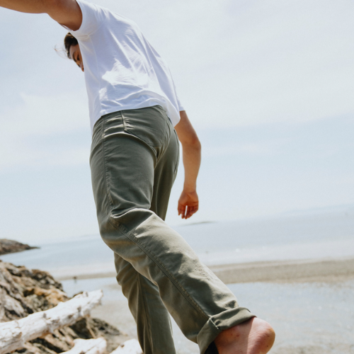 Person wearing a white shirt and green pants walking on a beach with a clear sky.