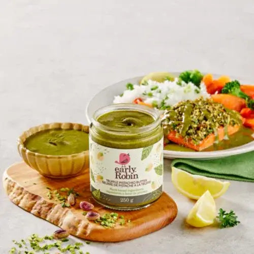 Jar of green spread on a wooden board with a plate of salad and salmon in the background.