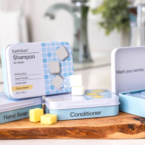 EarthSuds shampoo, conditioner, and hand soap packaging on a wooden surface with a blurred bathroom background.