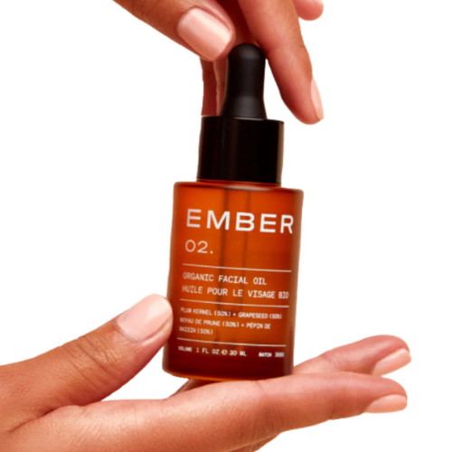 Hand holding a bottle of Ember organic facial oil against a white background