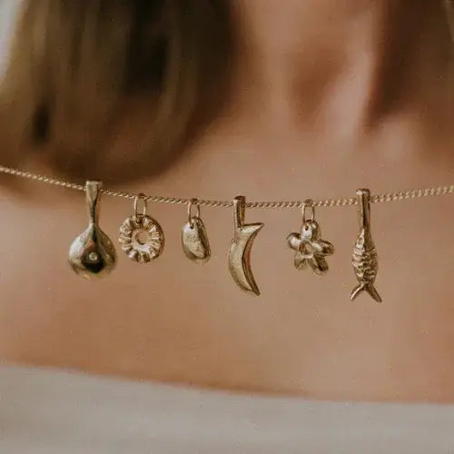 Close-up of gold charm necklace with handcrafted pendants including fig, flower, and fish – Artisanal jewellery by Canadian designer Emily Hartwell