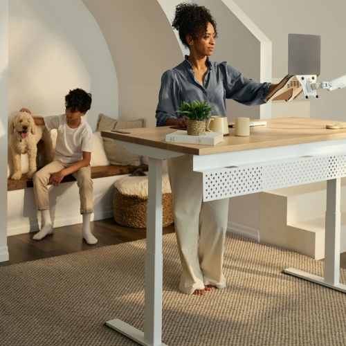 Woman standing at a modern desk with a child and dog in a home office setting.