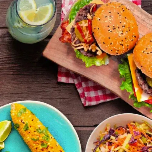 Hamburger on a wooden cutting board with a side of corn and salad, served on a wooden table.