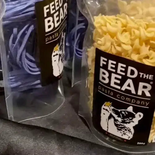 Packages of Feed the Bear pasta on a dark surface