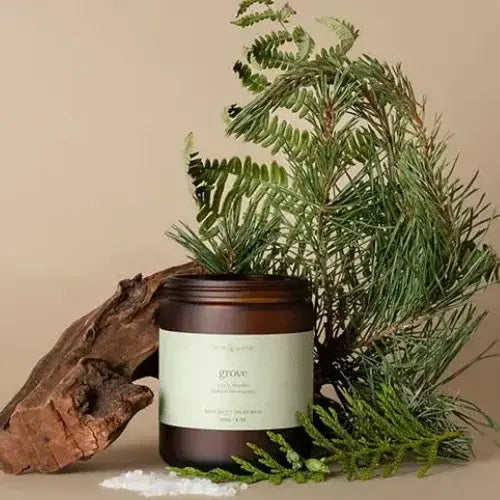 Candle in a brown jar with a label, surrounded by greenery on a beige background