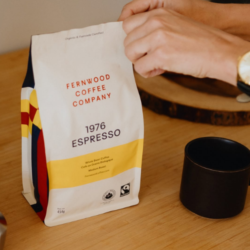 Fernwood Coffee Company 1976 Espresso bag held by a person with a black cup on a wooden surface.