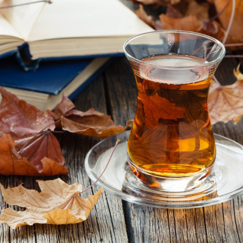 Glass of tea on a wooden surface with autumn leaves and an open book.