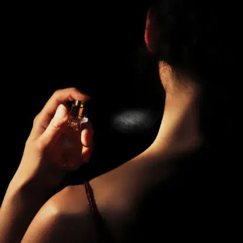 Person applying perfume to their neck against a dark background