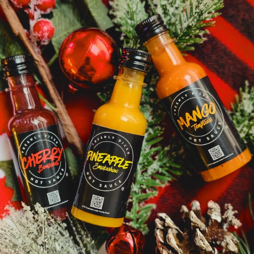 Three hot sauce bottles in cherry bomb, pineapple and mango flavours with holiday greenery