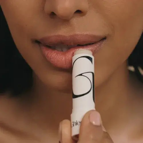 Close-up of a person applying a white lip balm with a black logo to their lips.