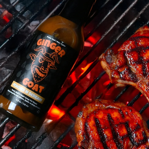 Bottle of 'Ginger Goat' sauce on a grill with grilled meat