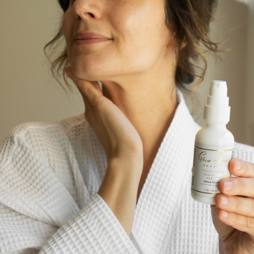 Woman in a white robe holding a skincare bottle with a neutral background