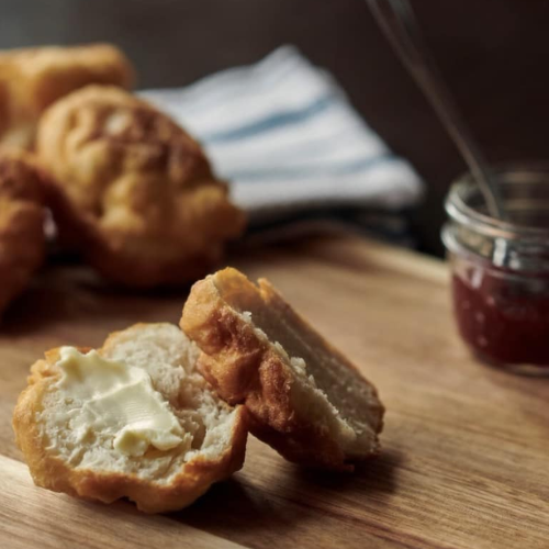 Bannock with butter on a wooden surface next to a jar of jam.