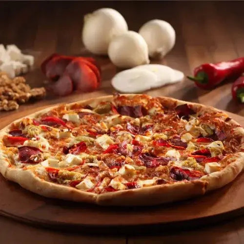 Personal-sized pizza with various toppings on a wooden board, surrounded by ingredients.