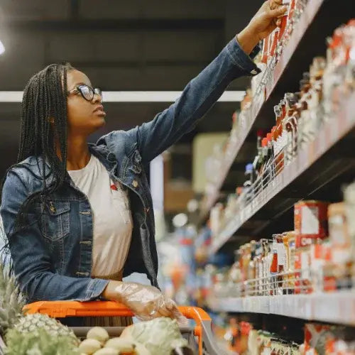 Woman grocery shopping in supermarket aisle with cart full of fresh produce – perfect for promoting Canadian-owned grocery and food brands.