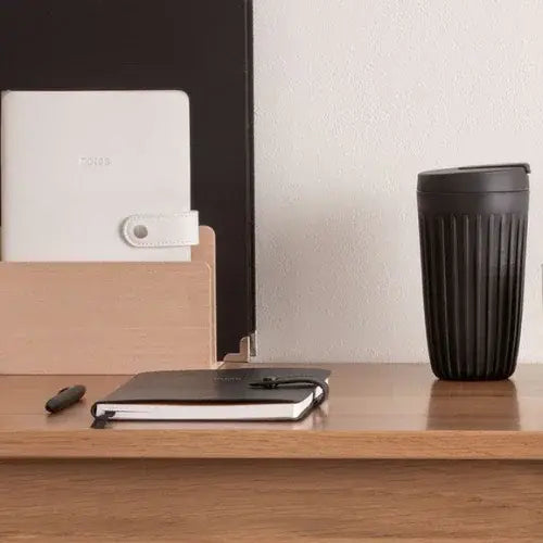 Black notebook, white notepad, and black mug on a wooden surface with a neutral background