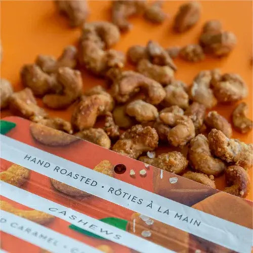 Hand roasted cashews spilling out of a package on an orange background
