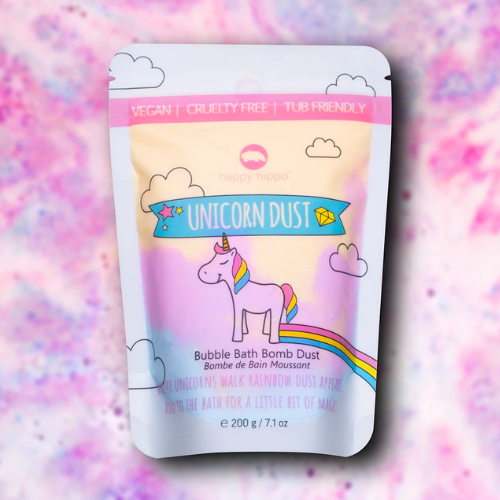 A stand-up pouch of Happy Hippo Unicorn Dust Bubble Bath Bomb Dust, featuring a pastel rainbow design with a cartoon unicorn and clouds, set against a matching pink and purple glittery background.