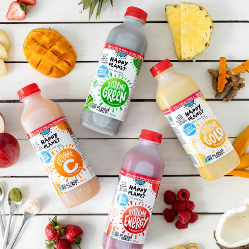 Happy Planet juice bottles on a wooden surface with fruits and ingredients