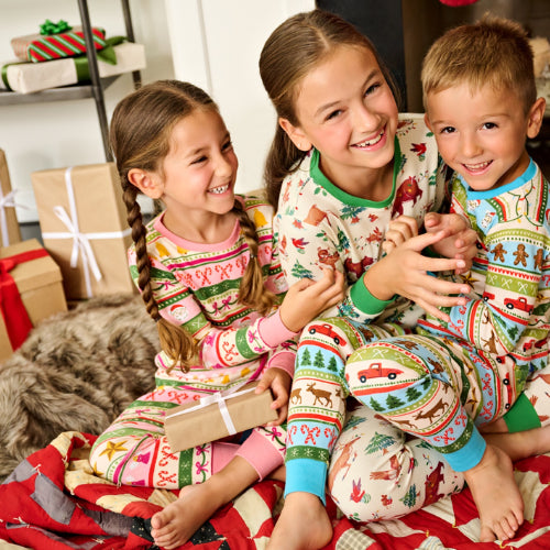 Three children in festive pajamas sitting together with Christmas presents around them.