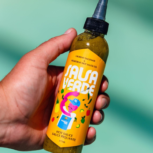 Hand holding a bottle of Sauce Verde hot sauce on a mint green background
