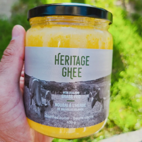 Jar of Heritage Ghee held by a hand with a blurred green background