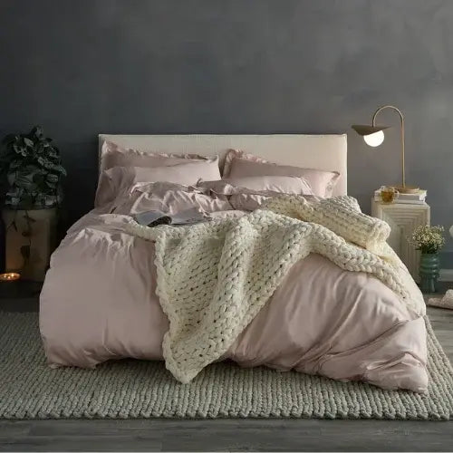 Bedroom with pink bedding and a knitted blanket on a bed against a dark wall.