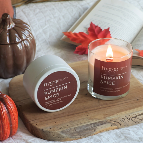 Hygge Pumpkin Spice candle and container on a wooden board with pumpkins and leaves.