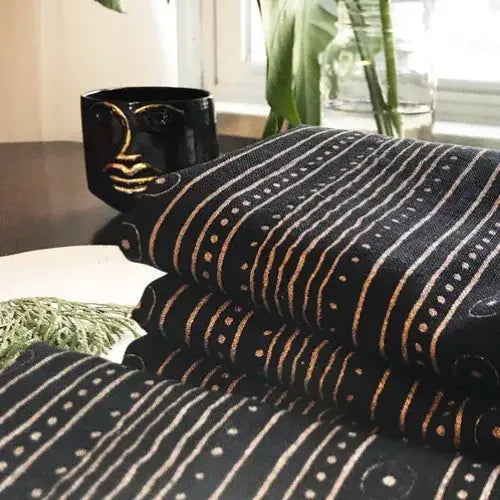Black and gold patterned fabric with a cup in the background