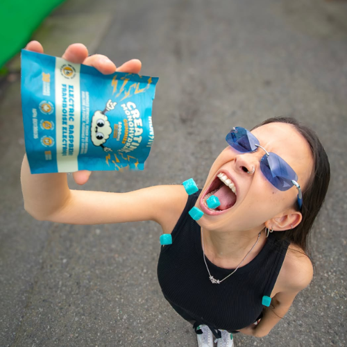 Person wearing sunglasses and blue Iron & Ivy creatine gummies, holding a blue snack package outdoors.
