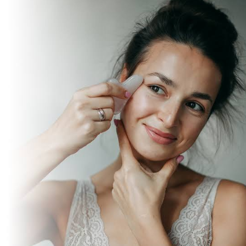 Woman applying cream to her face with a neutral background
