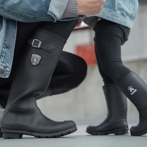 Two people wearing black rubber boots with visible brand logos on a blurred background.
