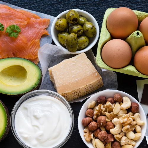 Assorted foods including avocados, eggs, nuts, and cheese on a dark surface.