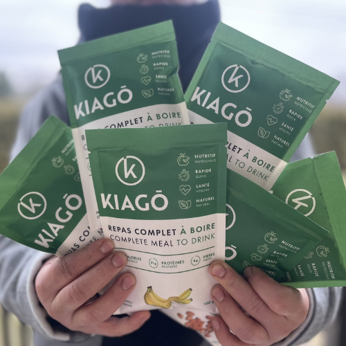Hands holding multiple green KIAGO meal replacement drink packages.