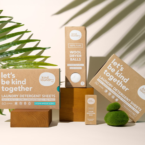 Kind Laundry eco-friendly products including dryer balls, detergent sheets, and a bar on a neutral background with a plant.