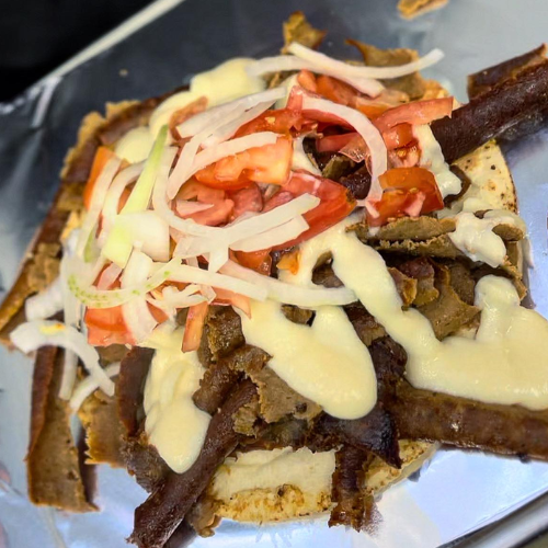 Stacked sandwich with beef, vegetables, and sauce on a white plate
