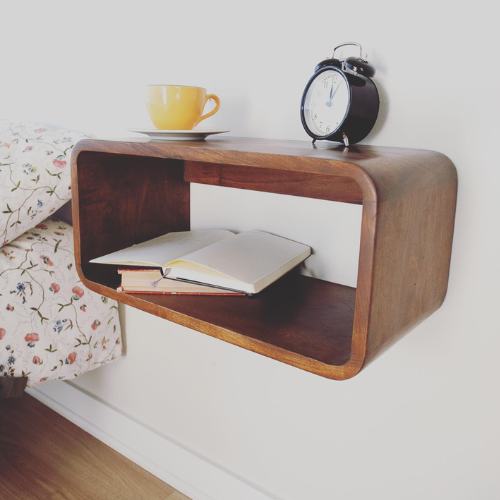 Wooden shelf with a book, yellow mug, and alarm clock on a white wall.