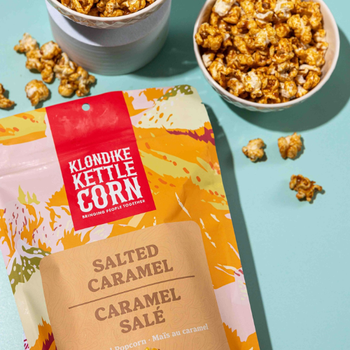 bag of klondike kettle corn labelled salted caramel with two bowls of popcorn in the background