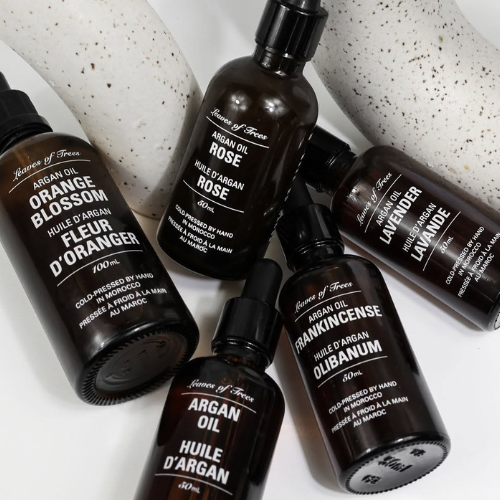 Six dark amber glass fragrance oil bottles from the brand 'Leaves of Trees' arranged on a white surface with two speckled ceramic props. 