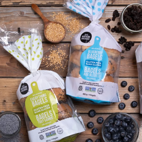 Two packages of Little Northern Bakehouse bagels on a wooden surface with various ingredients.