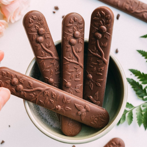 Chocolate sticks with embossed designs in a bowl on a light background
