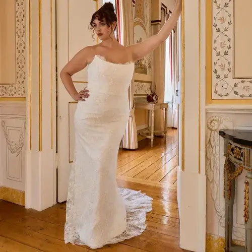 Woman in a white wedding dress standing in an ornate room with wooden floors and decorative walls.