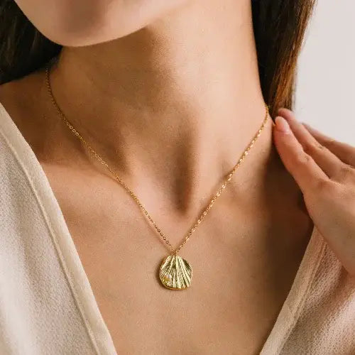 Gold necklace with a pendant worn by a person, against a neutral background